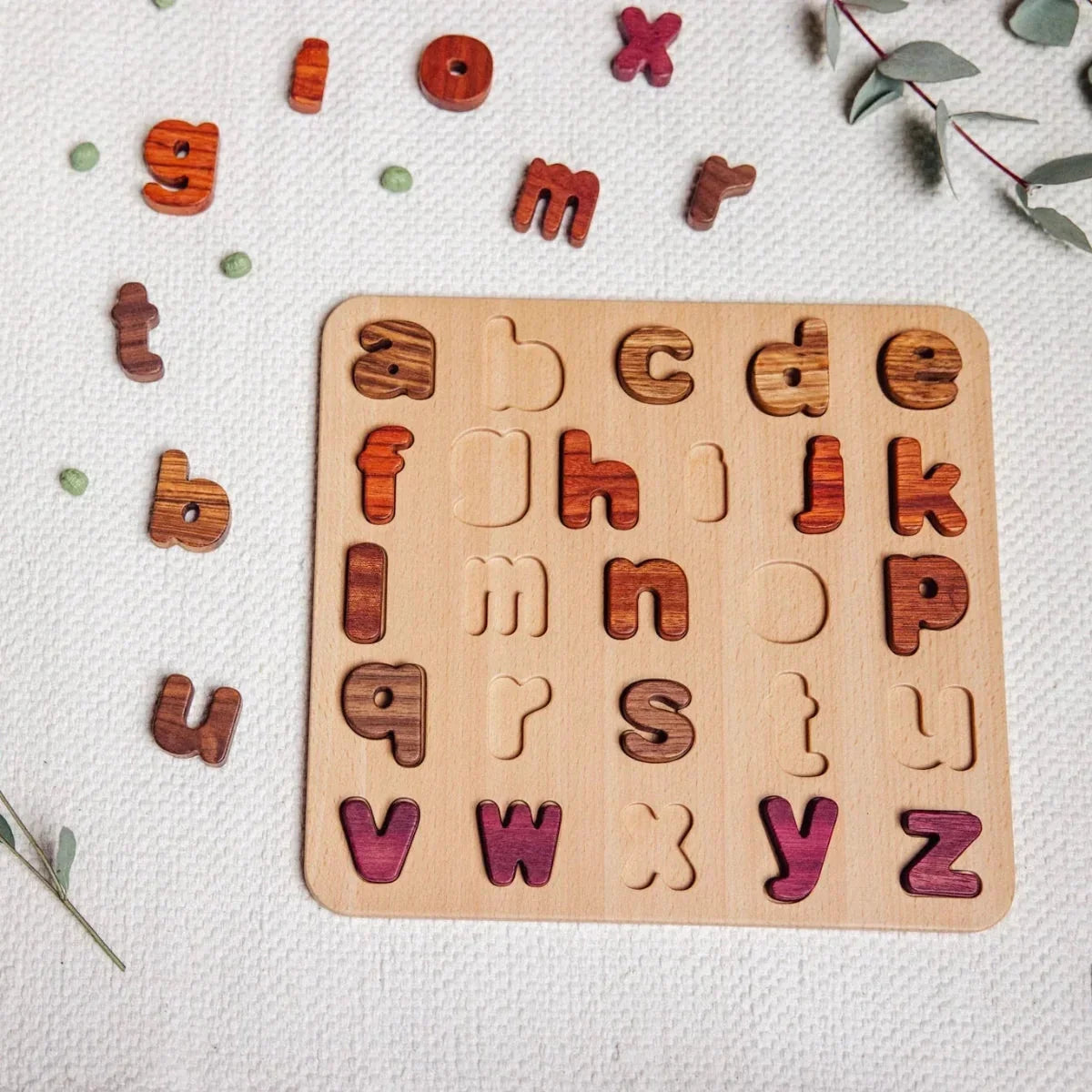 Oak & Sprout alphabet puzzle flat-lay with Padauk, Purpleheart and Walnut letters scattered on linen