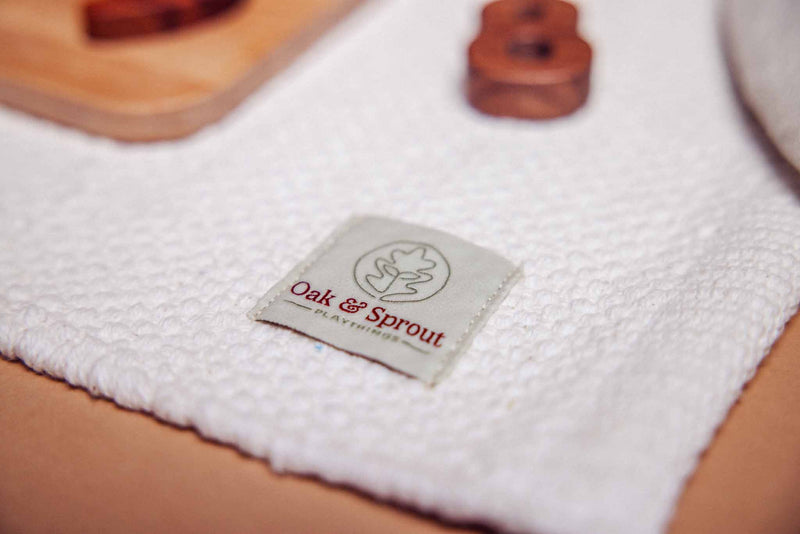 Oak & Sprout Playthings branded label on white textured playmat, walnut number puzzle pieces softly visible in background